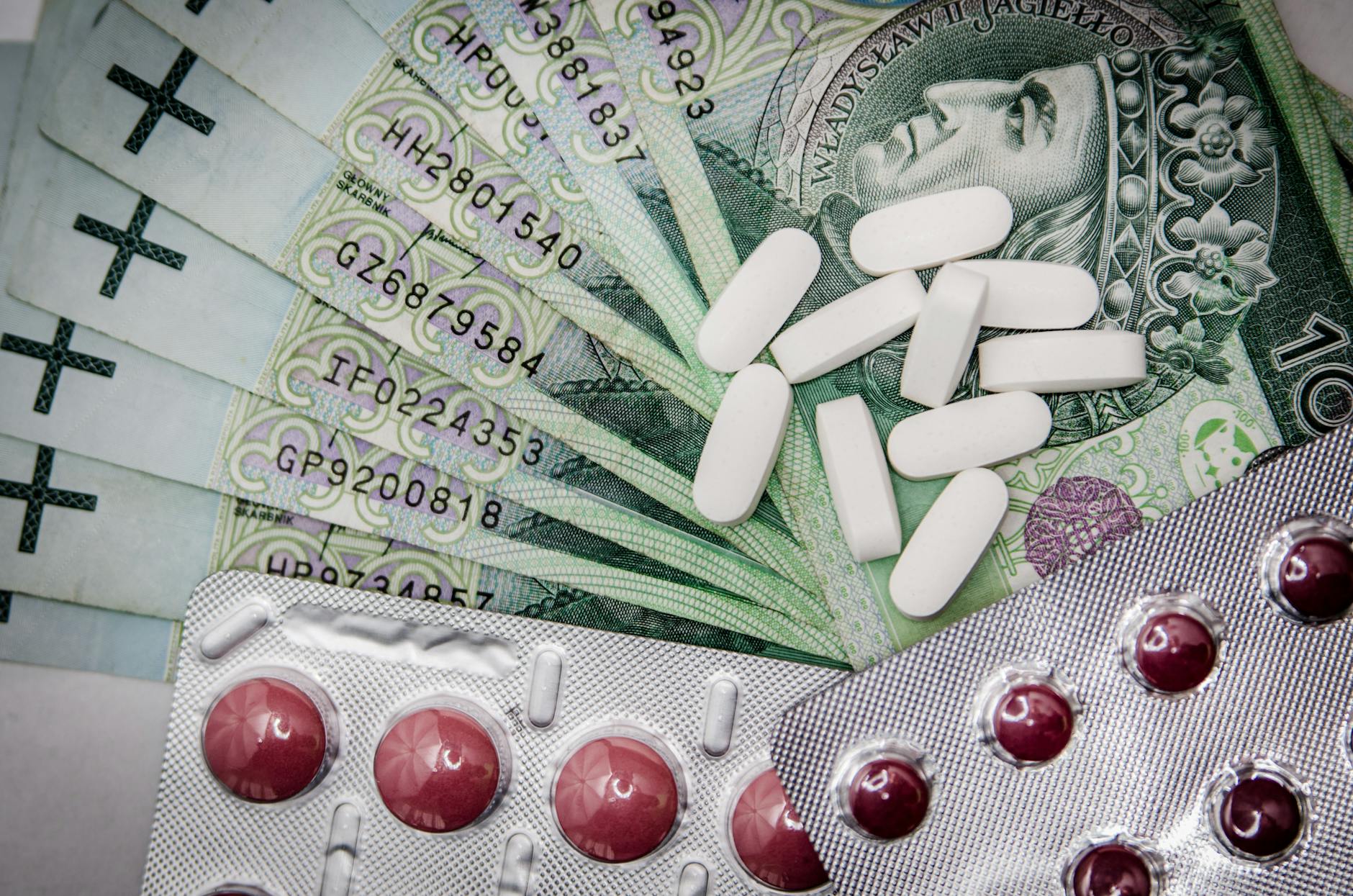 Banknot 100 zł obok tabletek i blistrów z lekami