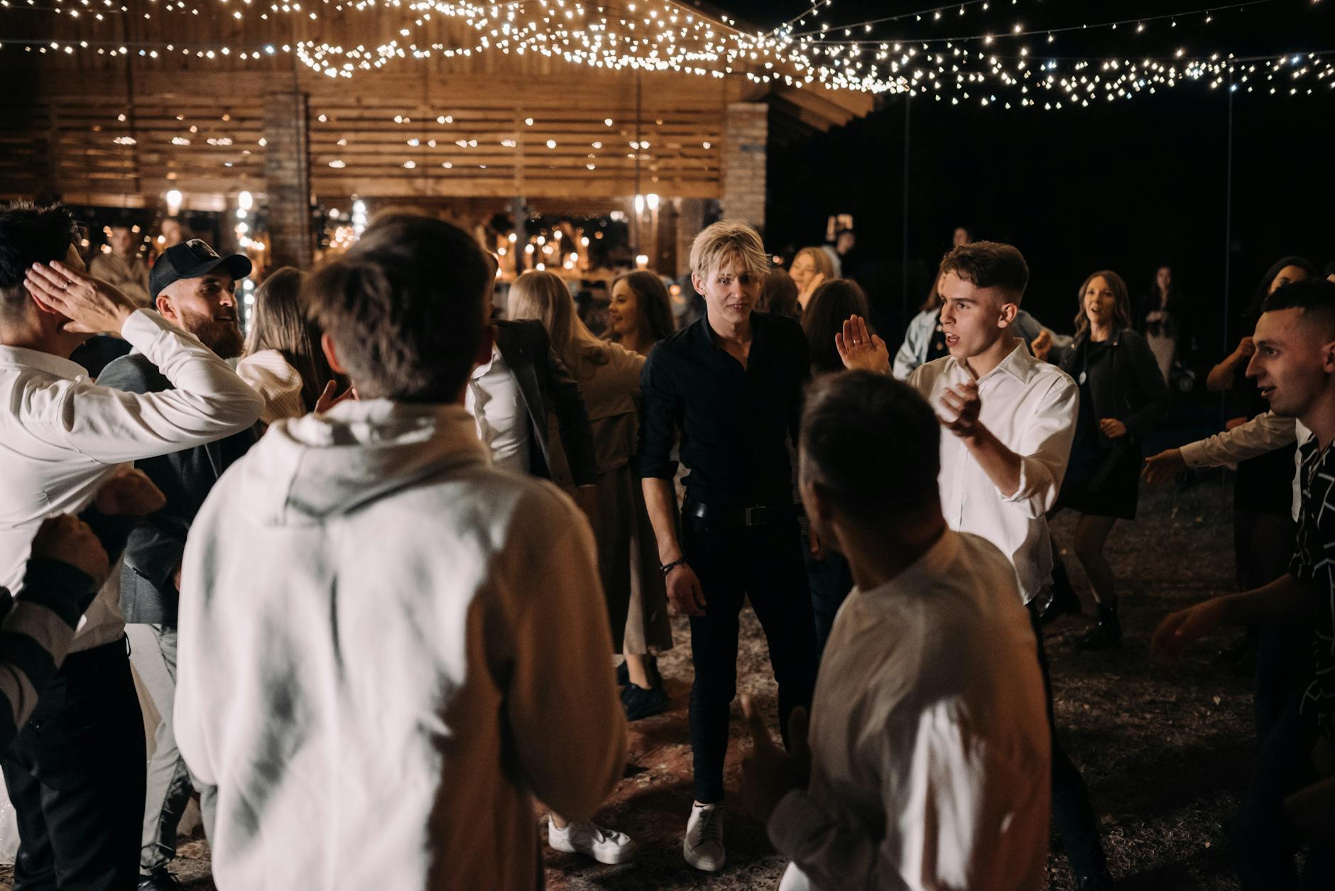 Goście tańczą pod lampkami na nocnym weselu plenerowym bez alkoholu