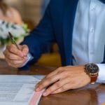 Co zrobić, gdy zespół weselny odwoła występ? Prawa pary młodej i odszkodowanie Pan młody podpisuje dokumenty ślubne obok panny młodej